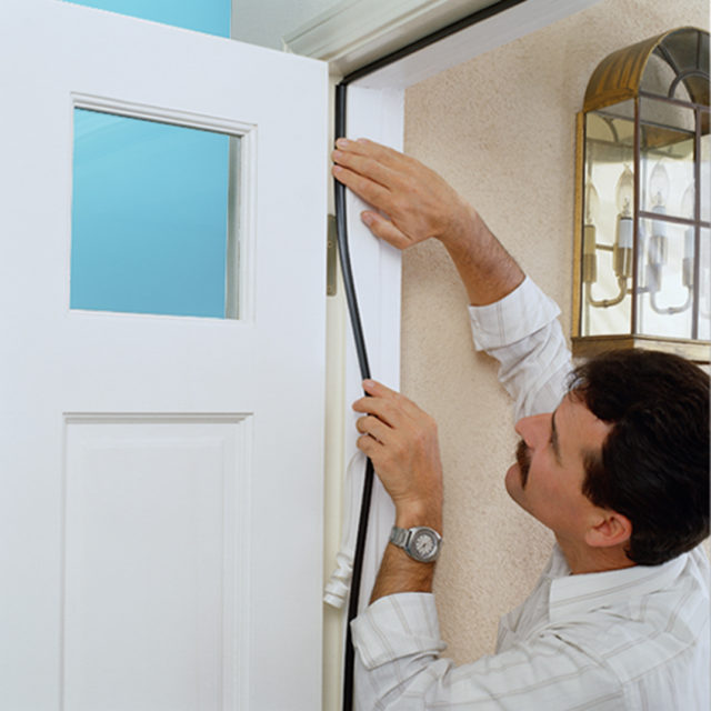 handyman adding weather stripping to door