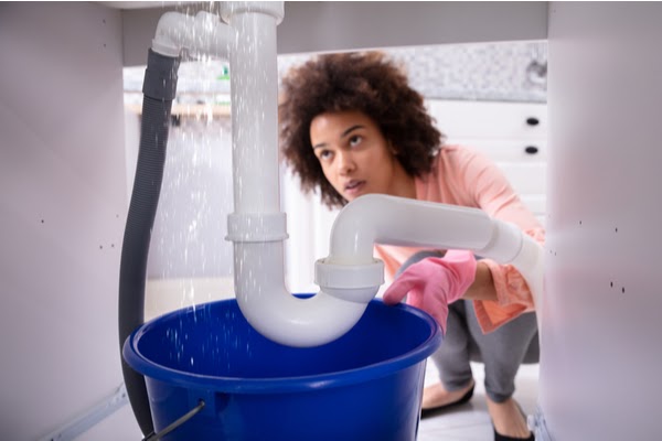 woman looking at leaking pipe under sink