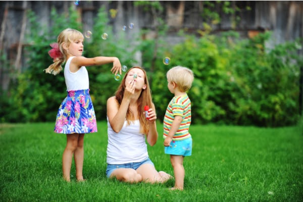 mother and two kids blowing bubbles on grass