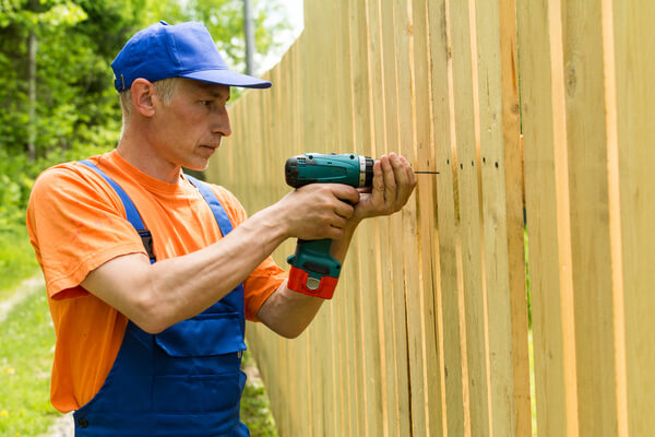 Carpenter twisting the screw in wooden board working at wooden fence outdoors