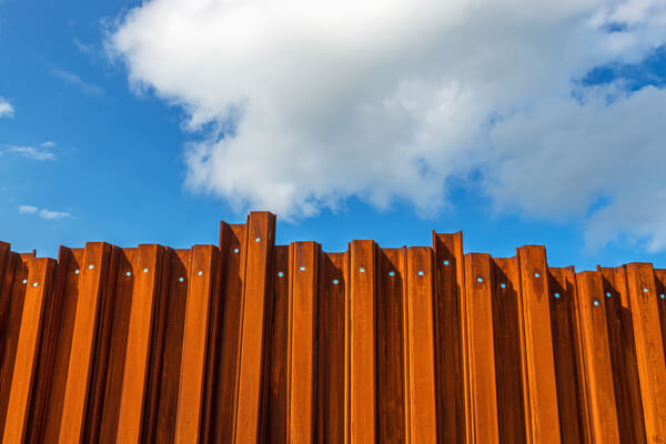 Tall rusty metal fence on the sandy beach with cloudy sky on the background