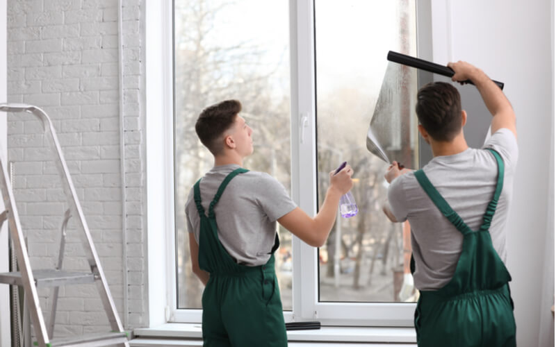 Professional workers tinting window with foil indoors