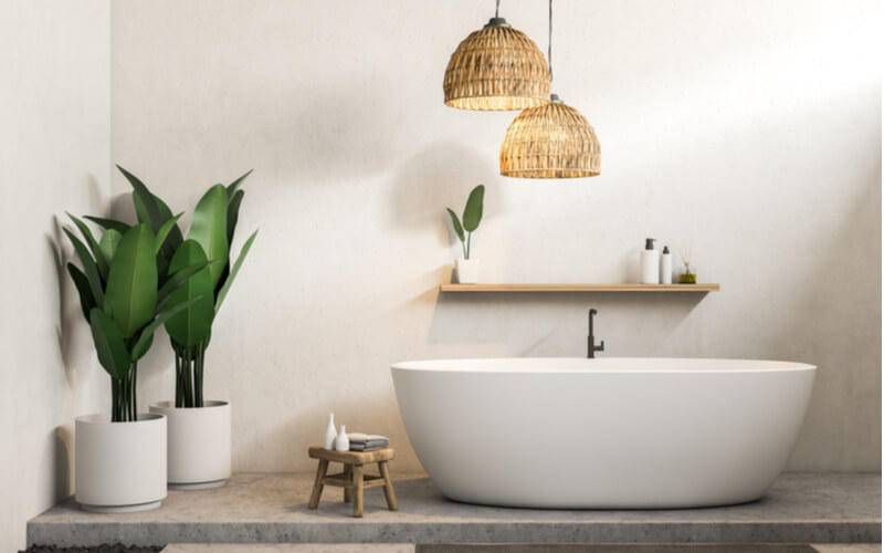 Interior of modern bathroom with white walls, concrete floor, white bathtub and shelf with creams and shampoo. Potted plants. 3d rendering