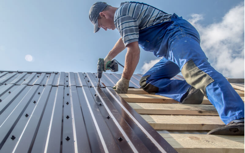 male builder performs work on the metal roof, fastens corrugated sheets