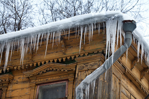 Frozen mysterious mansion with water pipe and frozen icicles on the roof, top floor wooden mansion. Icy weather winter scene