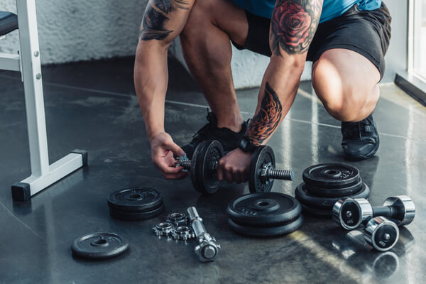 partial view of tattooed sportsman assembling dumbbells
