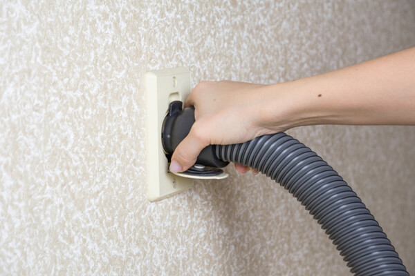 Woman hand holds the Central vacuum cleaner hose connected to the wall