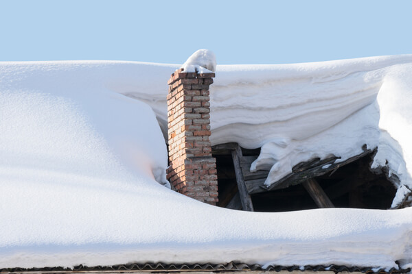 The roof collapsed under the weight of snow. Damaged falling roof and chimney on sunny day with clear blue sky.