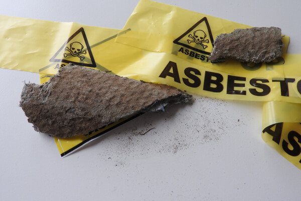 Close up of pieces grey asbestos and fibers. Roof tiles and yellow barrier tape. Warning: caution health effects, hazard. Asbest or asbestos removal. Asbestosis or mesothelioma.Cement, part serie