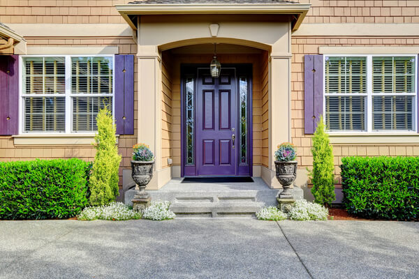 Luxury house. Clapboard siding exterior with purple elements. Entrance porch with trimmed hedges along the walls