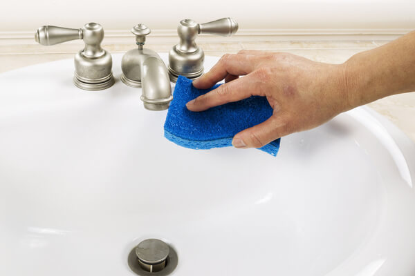 Hand with sponge cleaning bathroom sink faucet