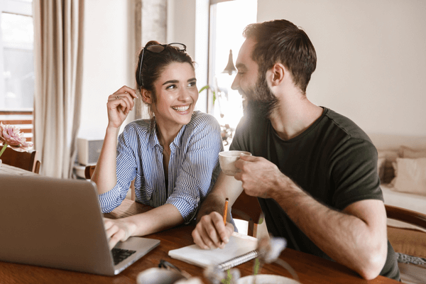 Image of successful brunette couple man and woman 20s drinking coffee and working on laptop together while sitting at table at home
