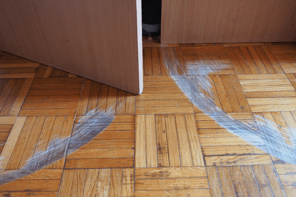 Scratched parquet flooring in the room. Scratches, chips and dents on the floor. Parquet in need of repair. Cabinet doors are scratching the floor. Unadjusted height of furniture doors.