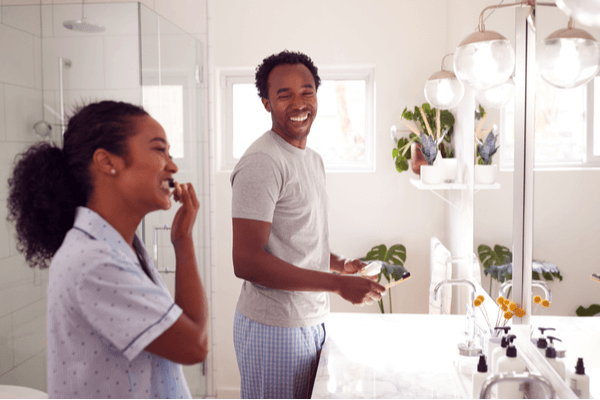 Couple Wearing Pyjamas Standing In Bathroom At Sink Brushing Teeth In The Morning