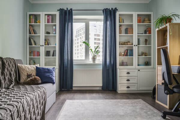 Светлая уютная комната для подростков с белыми книжными шкафами, серым диваном и голубыми стенами