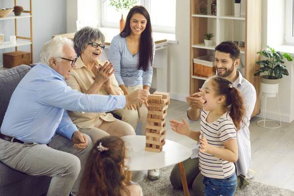 Happy big family with little children enjoying the weekend at home, playing board games and having a good time together. Excited grandkids having fun watching grandpa take a wood block from the tower