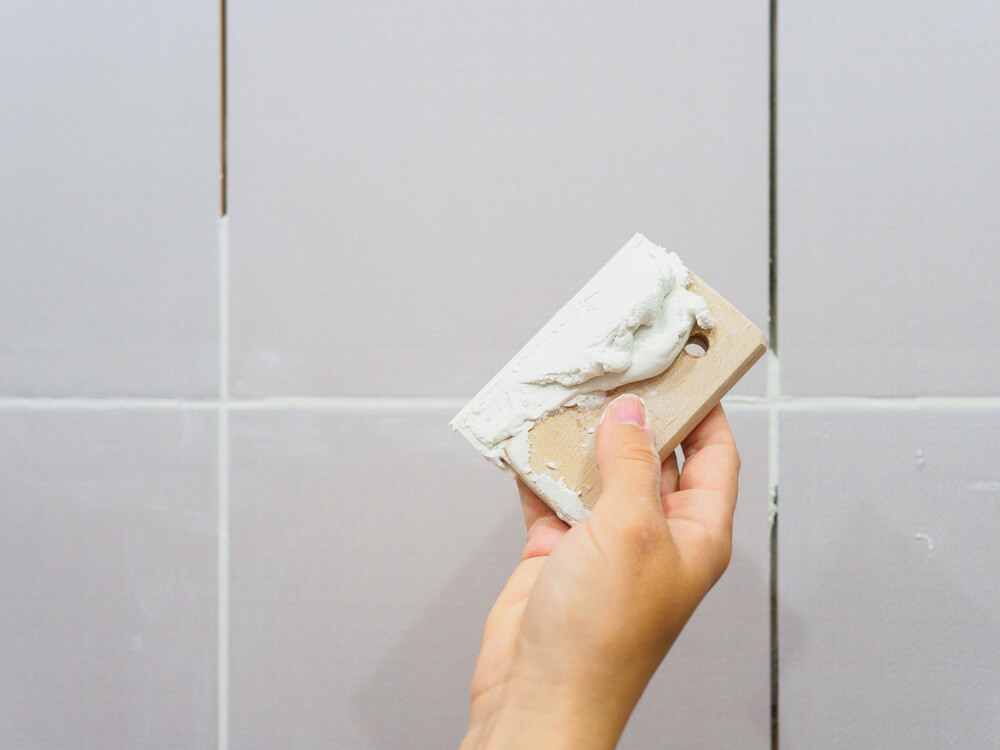 Grouting between tiles in the bathroom. Female hand holds a spatula. Repairs.