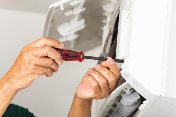 man using screwdriver to repair air conditioning