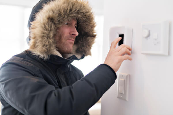 homeowner adjusting thermostat wearing winter coat